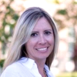A woman with long blonde hair, wearing a white shirt, is smiling outdoors with trees and sunlight in the background at the RSA 2024 event.